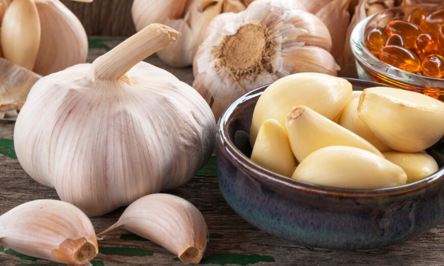 Garlic bulb, capsules oil extract in glass,  garlic cloves in green ceramic bowl, and on old wooden background, Garlic can help reduce the risk of many diseases. Classified as healthy food.
